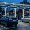 EV charging station business plan planning view: a modern DC fast-charging plaza at dusk with electric cars on green number plates