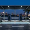 EV charging station design: four marked charging bays under a lit canopy with unbranded DC fast chargers and EVs on green number plates