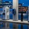 OCPP backend software managing five different EV charger models from different manufacturers at an urban charging plaza at dusk