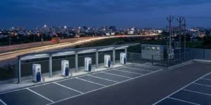 PM E-DRIVE charging station scheme: a newly built public DC fast charging hub beside an Indian city highway at dusk